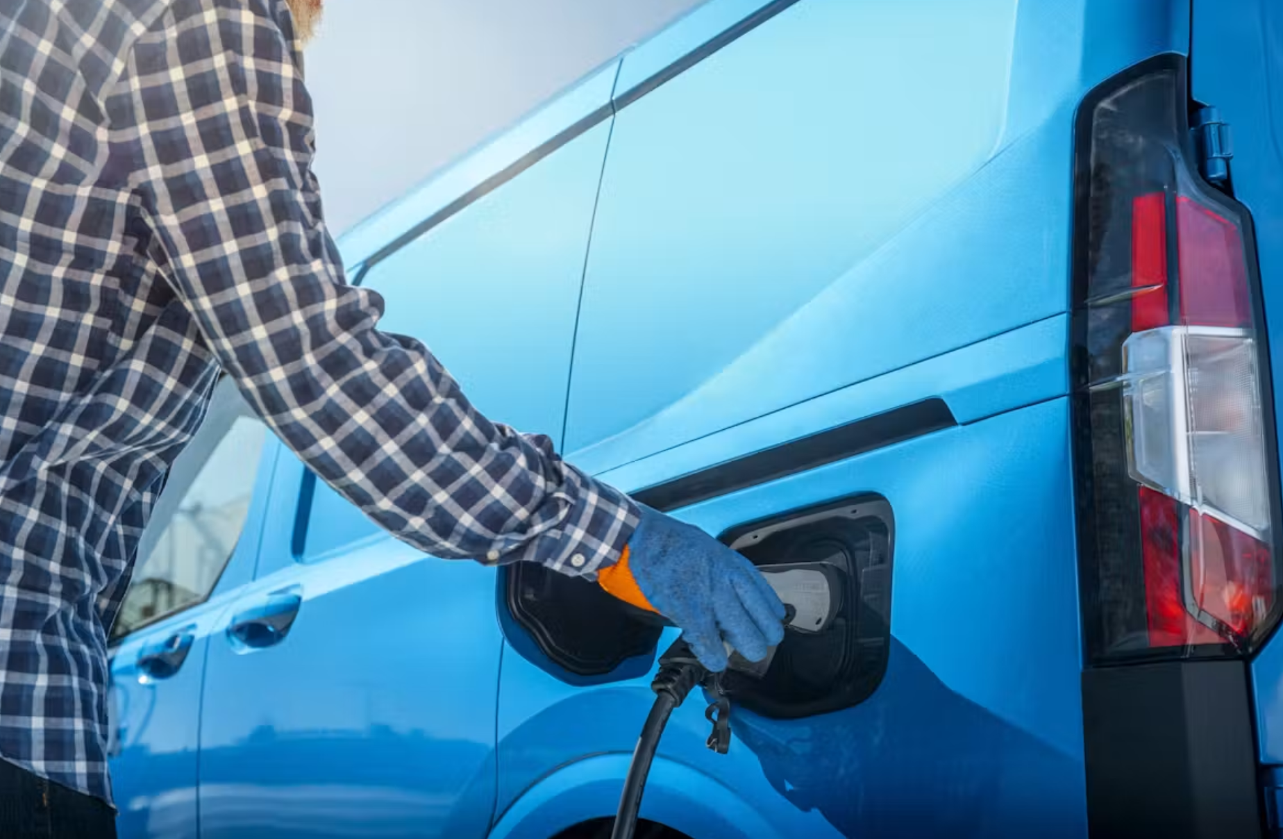 worker plugging in blue electric van to charge