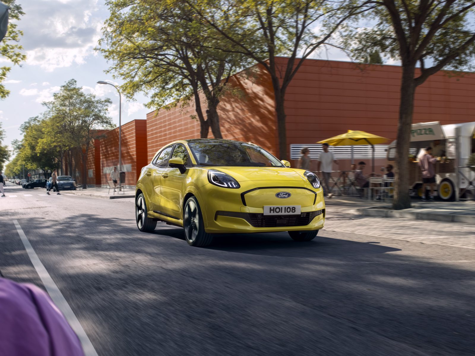 Ford Puma Gen e yellow electric car front profile with cafe in background
